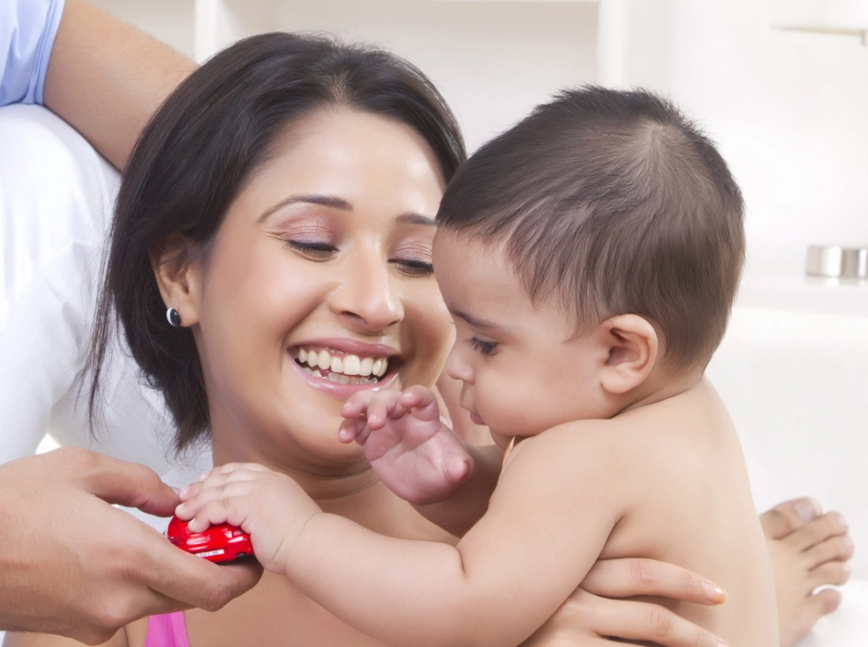 Woman smiling, holding baby and red heart. Image from Aveya Best IVF Centre Delhi.